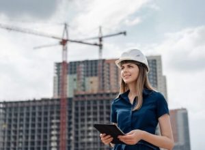 mulher loira de capacete branco e blusa azul com prédios ao fundo representando as mulheres na construção civil