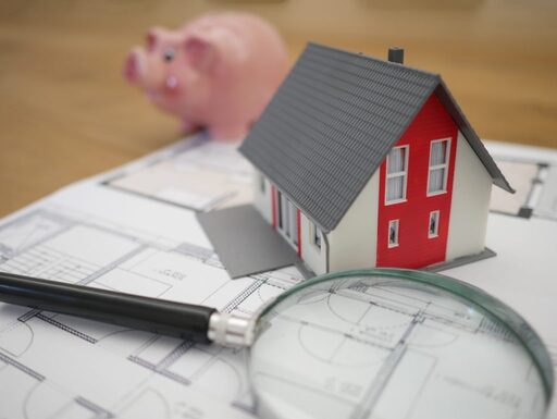 casa em miniatura em cima do projeto com uma lupa e um porquinho de cofrinho representando a oportunidade de economizar na obra